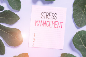 Ein Notizzettel mit der Aufschrift Stressmanagement umrandet von grünen Blättern als Anregung für gezieltes Stressmanagement Training