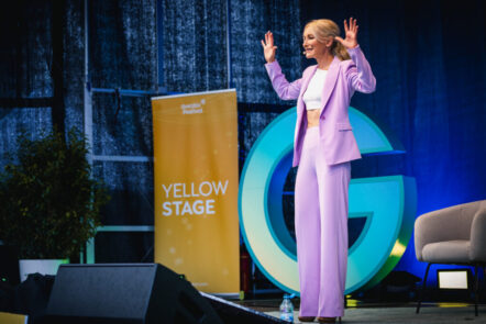 Beim Greator Festival steht Kerstin Hardt in einem lila Blazer auf der Bühne vor dem blauen Greator Logo