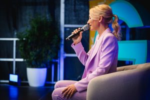 Kerstin Hardt in einem lila Anzug auf der blauen Greator Bühne bei ihrem Vortrag zu Produktivitätssteigerung