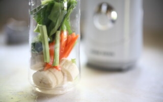 Banane, Karotte und grünes Gemüse im Glas im Vordergrund eines Mixers als Sinnbild der Erklärung für Wie geht Fasten
