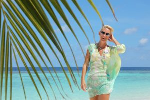 Kerstin Hardt vor einem Palmenblatt an einem weißen Sandstrand mit blauem Wasser zeigt wie leicht es ist, endlich wieder glücklich zu sein