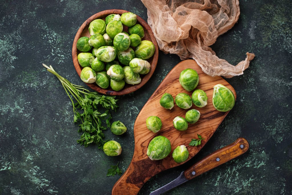 Grüner Rosenkohl auf einer schwarzen Oberfläche mit einem Holzbrett steht sinnbildlich für die Grundlagen der Ernährung 