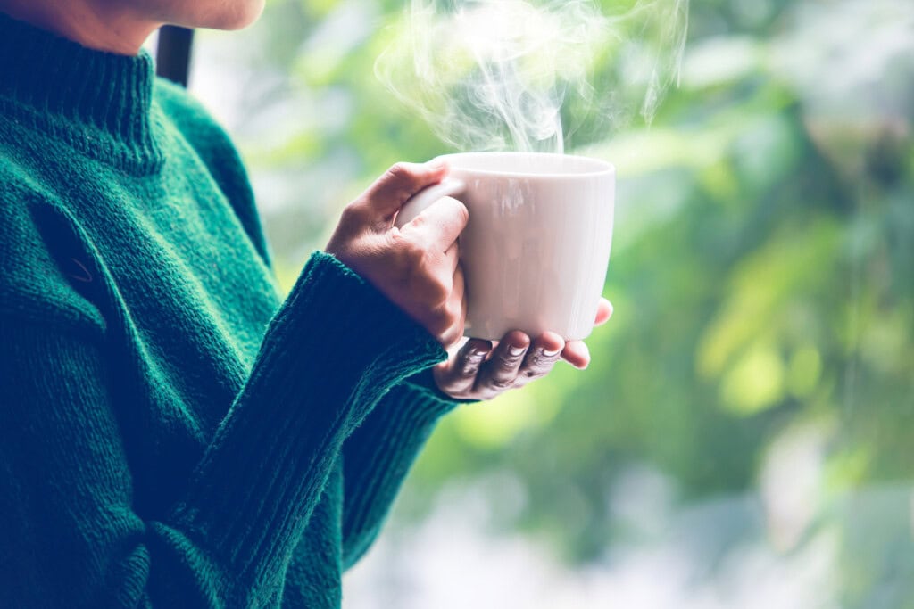 Das Bild einer Frau im grünen Pulli, die eine dampfende weiße Tasse hält, steht sinnbildlich für Mentale Gesundheit am Arbeitsplatz