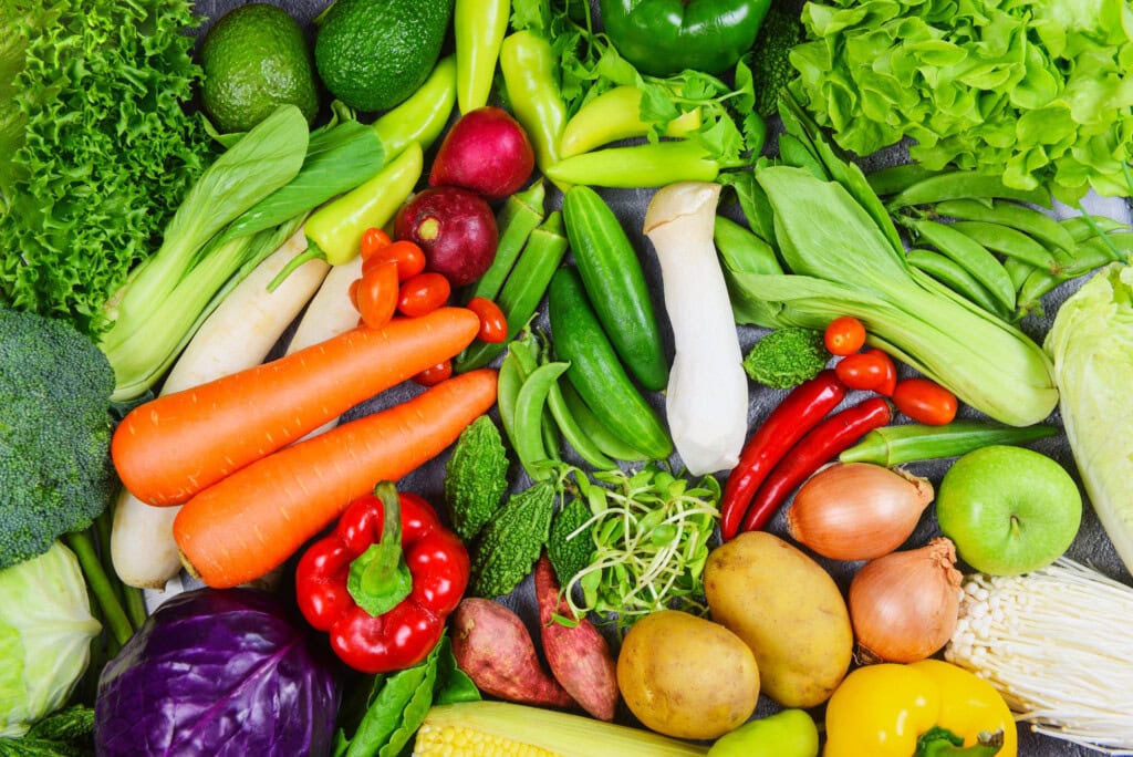 Eine bunte Mischung Gemüse, unter anderem Karotte, Paprika, Kartoffeln und Salat, von oben zeigt, dass ganzheitliche Ernährung alles andere als einseitig ist