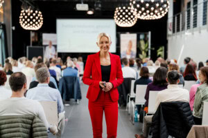 Kerstin Hardt bei Energize your Life in einem rote Anzug vor einer Menschenmenge zeigt, wie Produktivitätssteigerung geht. 