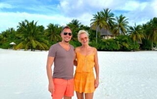 Kerstin und Ihr Mann Marco in Somemrkleidung an einem weißen, tropischen Strand zeigen, wie glückliche Beziehungen funktionieren