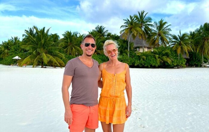 Kerstin und Ihr Mann Marco in Somemrkleidung an einem weißen, tropischen Strand zeigen, wie glückliche Beziehungen funktionieren