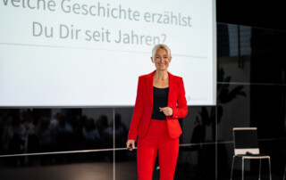 Kerstin Hardt steht in einem roten Anzug auf der Bühne, das Mikrofon in der Hand und erzählt alles über das beste Mittel zur Stärkung des Immunsystems