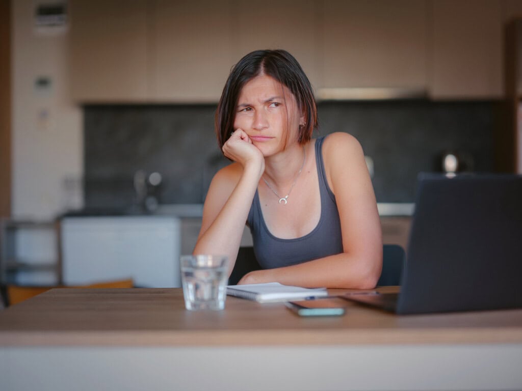 Eine junge Frau mit dunklen, kurzen Haaren sitzt mit einem frustrierten Gesichtsausdruck for ihrem Computer. Sie will ihren Brain Fog behandeln, aber wieß nicht wie. 