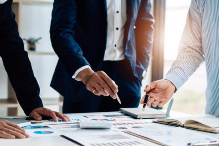 Eine Gruppe von Menschen steht über einem Tisch mit Plänen als Sinnbild für Stressmanagement Training