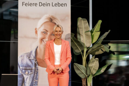 Kersin Hard in einem lachsfarbenen Kostüm vor einem ihrer Plakate erklärt, wie leicht Stoffwechsel anregen geht